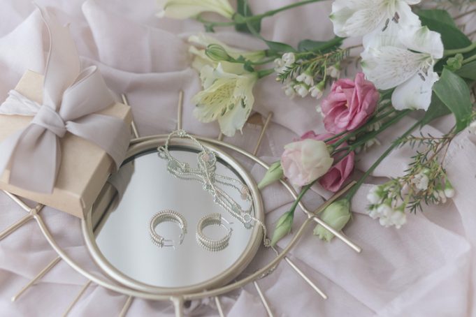 Stylish gift box, modern jewelry, spring bouquet on boho mirror